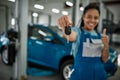 It is done. Young african american woman, professional female mechanic smiling at camera, giving car key and showing Royalty Free Stock Photo