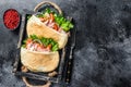 Doner kebab with grilled chicken meat and vegetables in pita bread on a wooden tray. Black background. Top view. Copy space Royalty Free Stock Photo
