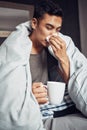 Dont get the flu, get the shot. Shot of a young man blowing his nose and having tea while recovering from an illness in Royalty Free Stock Photo