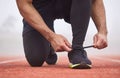 Dont wanna trip over these. an unrecognizable male athlete tying his laces out on the track.