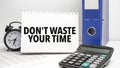 dont waste your time words on white notebook and calculator, black vintage alarm clock and blue paper folder