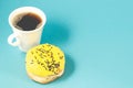 Donut and coffe cup on blue background/Donut in yellow glaze decorated with dark chocolate sticks and coffe cup isolated blue