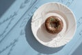 Donut covered with chocolate glaze and sprinkled with green tubes on white plate on blue background Royalty Free Stock Photo