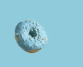 Donut covered with pale blue icing and sprinkled with pearl sugar beads on a light blue background. Closeup