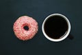 Donut in pink glaze and cup of coffee on dark background, view from above Royalty Free Stock Photo