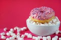 Donut in pink glaze with sprinkles next to small marshmallows and a white plate Royalty Free Stock Photo
