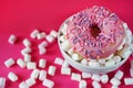 Donut in pink glaze with sprinkles next to small marshmallows and a white plate Royalty Free Stock Photo