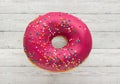 Donut pink with sprinkles isolated on wooden background, close-up Royalty Free Stock Photo