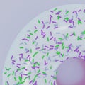 Donut quarter with white glaze and multicolored pastry sprinkles in green, blue and purple color on light gray violet background.