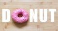 Donut text with pink donut instead of `O` letter, on wooden table.