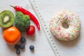 Donut vs. fruits and vegetables on white wooden background and tape measure, diet and calories concept Royalty Free Stock Photo