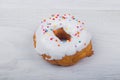 Donut with white glaze on white wooden background