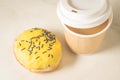donut in yllow glaze and a paper coffee cup/donut in yellow glaze and a paper coffee cup on a white table. Top view