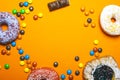 Donuts with colored icing and bun cherries with powdered sugar .colored chocolate sweets on an orange background copy space