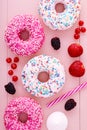 Donuts, fresh fruits, marshmallow and a straw on pastel pink wooden table background