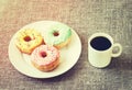 Donuts with a glaze on a white plate. Nearby is a coffee mug