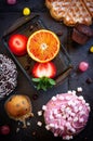 Donuts and muffins with fruit on black stone background.