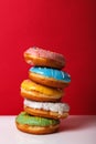 Donuts in multi-colored glaze stacked on top of each other on a red background, copy space. Bakery advertising concept