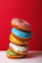 Donuts in multi-colored glaze stacked on top of each other on a red background, copy space. Bakery advertising concept