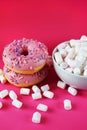 Donuts in pink glaze with sprinkles next to small marshmallows and a white plate Royalty Free Stock Photo