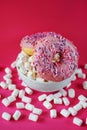 Donuts in pink glaze with sprinkles next to small marshmallows and a white plate Royalty Free Stock Photo