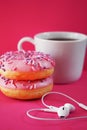 Donuts in pink glaze with sprinkles next to a white cup of coffee and headphones laid out in the shape of a heart Royalty Free Stock Photo