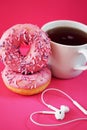 Donuts in pink glaze with sprinkles next to a white cup of coffee and headphones laid out in the shape of a heart Royalty Free Stock Photo