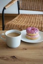 Donuts with pink icing and a cup of coffee with milk on a wooden table against the background of a chair Royalty Free Stock Photo