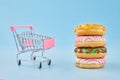 Donuts on small shopping cart. Shopping trolley and glazed doughnut on blue pastel background. Unhealthy food Royalty Free Stock Photo