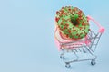 Donuts on small shopping cart. Shopping trolley and glazed doughnut on blue pastel background. Unhealthy food. Royalty Free Stock Photo