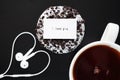 Donuts in white glaze with chocolate sprinkles next to a white cup of coffee and headphones laid out in a heart shape Royalty Free Stock Photo