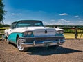 A 1958 door Buick sedan in turquoise and white. Parked in a rural setting on a sunny day with countryside in the background