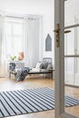 Door and carpet in white minimal bedroom interior with poster above bed next to window Royalty Free Stock Photo