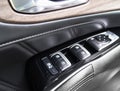 Door handle with power window control buttons of a luxury passenger car. Black perforated leather interior with stitching. Modern