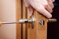 Door installation, worker Installs door knob, woodworker hands close up. A man spins the door handle with a screwdriver, repairs Royalty Free Stock Photo