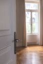 Door knob on white retro door, close up. Door open, blur room interior, window and wood floor Royalty Free Stock Photo