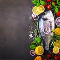 Dorada, fresh fish with vegetable, lemon, herbs, onion, paprika, cherry tomatoes, onion, salton dark vintage background. Copy spac Royalty Free Stock Photo