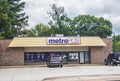 View of a Metro PCS store and sign with a parked car and green trees