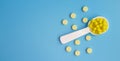 A dosed spoon filled with yellow vitamin C on the background of tablets. Free space for text