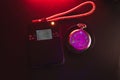 Dosimeter of radioactive radiation next to an old pocket watch with dangerous fluorescent paint. Violet light and green glow of