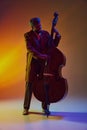 Double bass player, African-American man in retro attire performing neon light against gradient background.