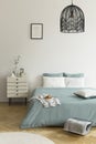 A double bed with sage green and white bedding standing on a wooden floor in a bright bedroom interior. A nightstand next to the b