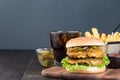 Double cheese burger with caramelized onion, lettuce and jalapeno, served with french fries and soda, on wooden board, horizontal