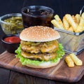 Double cheese burger with caramelized onion, lettuce and jalapeno, served with french fries and soda, on a wooden board, square Royalty Free Stock Photo