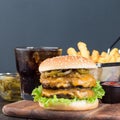 Double cheese burger with caramelized onion, lettuce and jalapeno, served with french fries and soda, on a wooden board, square Royalty Free Stock Photo