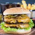 Double cheese burger with caramelized onion, lettuce and jalapeno, served with french fries and soda, on wooden board, square Royalty Free Stock Photo