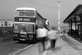 Double decker Leyland Olympian preserved bus at bus stop. Ghostly blurred passengers wait to board and travel. Black and white