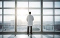 Double exposure of confident doctor in white sterile coat standing inside hospital office and modern cityscape view on