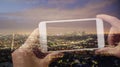 Double exposure of hands holding a mobile phone and taking a picture of cityscape Los Angeles at night