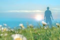 A double exposuref a close up of blurred daises Bellis perennis in a meadow, with a hiker looking at the sunset. With a dream